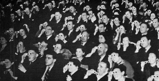 Vintage black and white image of a crowd in a movie theatre wearing cardboard 3D glasses and staring towards a screen